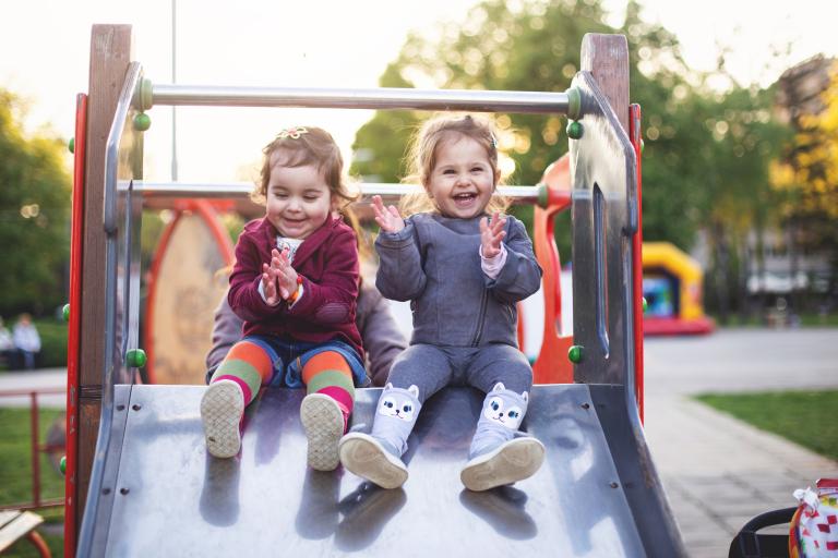 two young children sitting on a slide in a park 