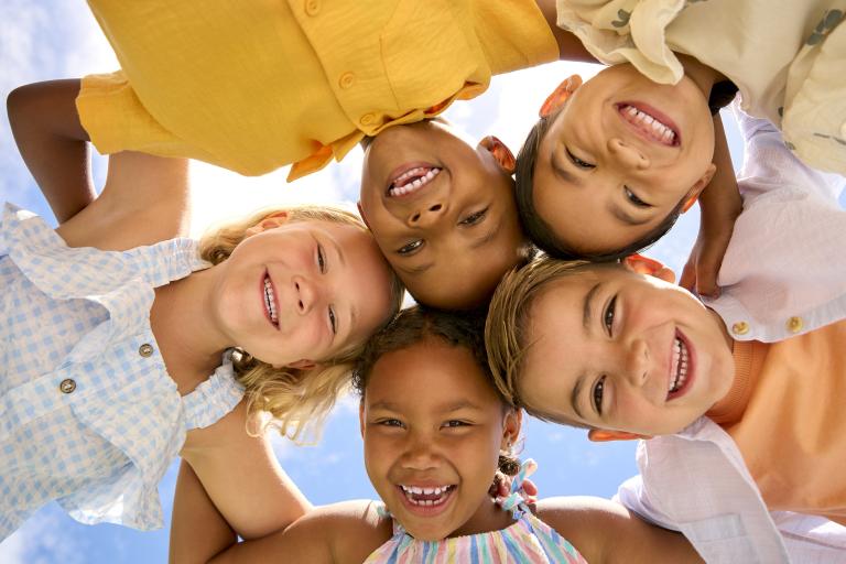 Group Of Children Friends Linking Arms Looking Down Into Camera